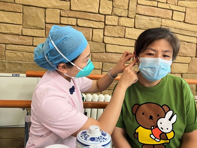图为护理人员为社区居民进行耳豆贴穴治疗